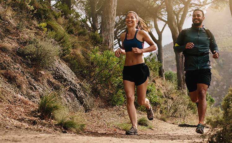 a happy, pain-free couple running on a trail in the woods