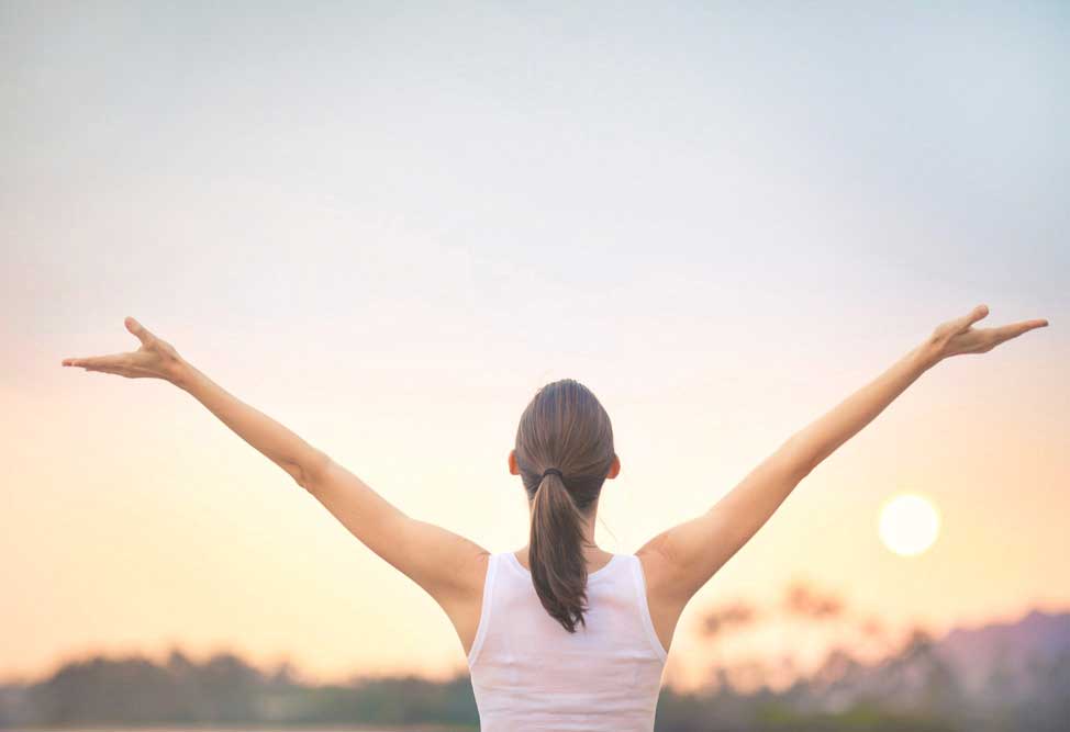 a healthy woman facing the sunrise while stretching her arms up